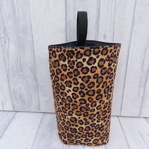 Puede incluir: Una bolsa de almacenamiento de tela con estampado de leopardo con un asa negra. La bolsa est&aacute; hecha de una tela suave y duradera y es perfecta para guardar objetos peque&ntilde;os.