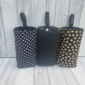 Puede incluir: Tres bolsas de almacenamiento de tela colgantes con tela negra y diferentes patrones. La bolsa de la izquierda tiene lunares blancos, la bolsa del medio es negra s&oacute;lida y la bolsa de la derecha tiene lunares dorados.