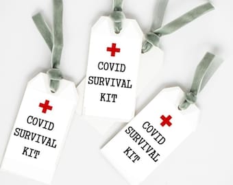 May include: White gift tags with the text "COVID SURVIVAL KIT" in black, topped with a red cross symbol. Each tag is tied with a gray ribbon. The tags are arranged on a white surface.