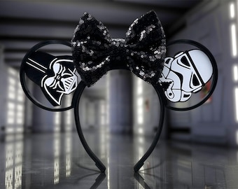 Pode incluir: Faixa de cabeça de orelhas de Minnie Mouse com tema Star Wars em preto e branco com um laço preto e uma imagem de Darth Vader em uma orelha e uma imagem de Stormtrooper na outra orelha.