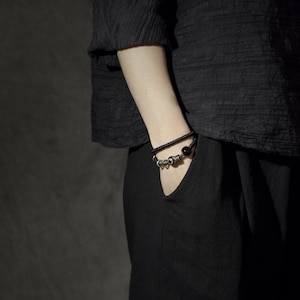 May include: A person wearing a black shirt and black pants with a black and silver beaded bracelet on their wrist.