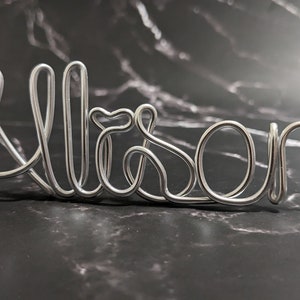 May include: Silver wire name art spelling out the name "Alison".