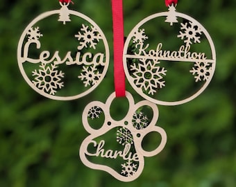 May include: Three wooden Christmas ornaments with snowflake designs. The ornaments are personalized with the names "Jesscia", "Kohnathon", and "Charlie".