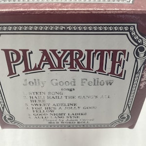 May include: A vintage box with the word "PLAYRITE" in maroon letters. The box is labeled "Jolly Good Fellow" and lists song titles including "Stein Song" and "Sweet Adeline". The box is trimmed with decorative borders.