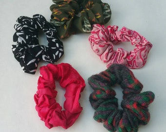 May include: Five colorful hair scrunchies in different patterns and fabrics. The scrunchies are made of a variety of materials, including cotton, velvet, and fleece. They are all in different colors, including black, green, pink, red, and white.