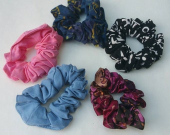 May include: Five colorful hair scrunchies in a variety of patterns and colors. The scrunchies are made of fabric and have a gathered, ruffled look.