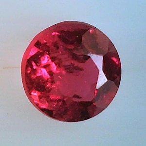 May include: Two round, red gemstones with a faceted cut. The gemstones are set against a white background.