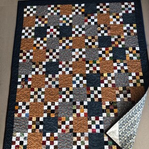 May include: A patchwork quilt with a blue background and a variety of colourful squares. The quilt is made of different fabrics and patterns, including plaid, floral, and geometric designs. The quilt is folded in half and the back side is visible.