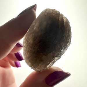 May include: A smoky grey quartz crystal with a rough, natural texture. The crystal is translucent and has a slightly iridescent sheen.