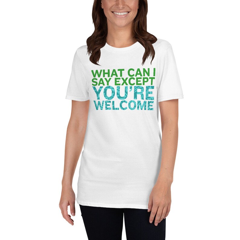 Puede incluir: Camiseta blanca con texto verde y azul que dice "What can I say except you're welcome".