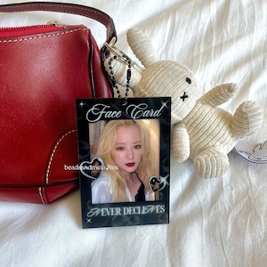 May include: A rectangular black acrylic photo holder featuring the white text Face Card at the top and NEVER DECLINES at the bottom. The frame includes two small heart-shaped cutouts and displays a portrait of a person with blonde hair.
