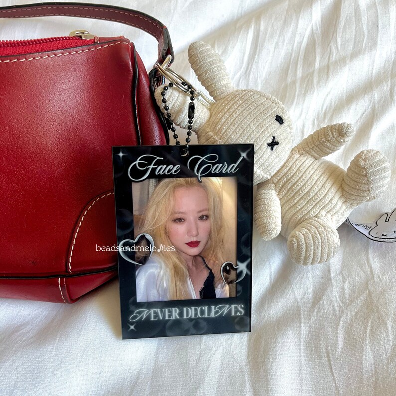 May include: A rectangular black acrylic photo holder featuring the white text Face Card at the top and NEVER DECLINES at the bottom. The frame includes two small heart-shaped cutouts and displays a portrait of a person with blonde hair.