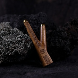May include: A wooden smoking pipe with a carved design and a brass accent. The pipe is shaped like a branch with a small bowl at the end.