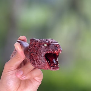 May include: A wooden pipe carved in the shape of a snarling animal head with a red finish and white teeth.