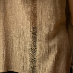 May include: A tan hooded shirt with a vertical distressed detail down the center back. The fabric has a textured appearance. The shirt's design is simple and casual, suitable for everyday wear. The hood is visible at the top of the image.