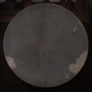 May include: A dark gray round drum with a slightly textured surface. The drum has a worn look with some light gray spots.