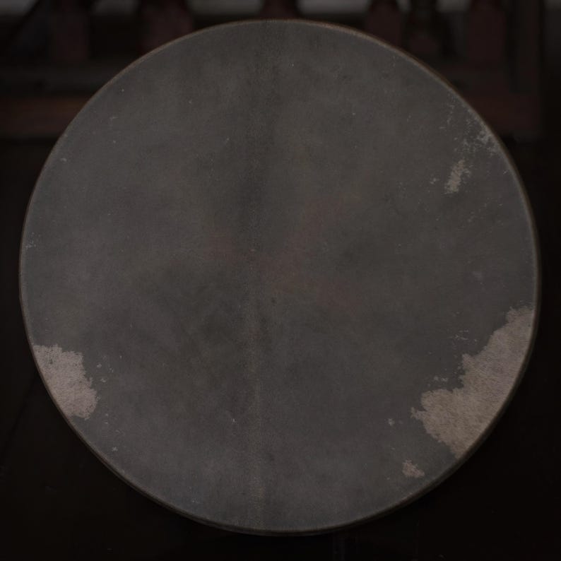 May include: A dark gray round drum with a slightly textured surface. The drum has a worn look with some light gray spots.