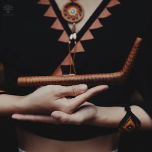 May include: A person holding a long, brown wooden pipe with a curved end. The pipe has a textured surface and appears to be handcrafted.