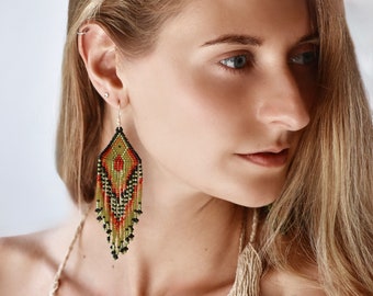 May include: A pair of long, diamond-shaped dangle earrings crafted from small glass beads in shades of olive green, vibrant red, and black. The earrings feature a geometric pattern at the top with a long, multi-strand fringe of beads hanging below.