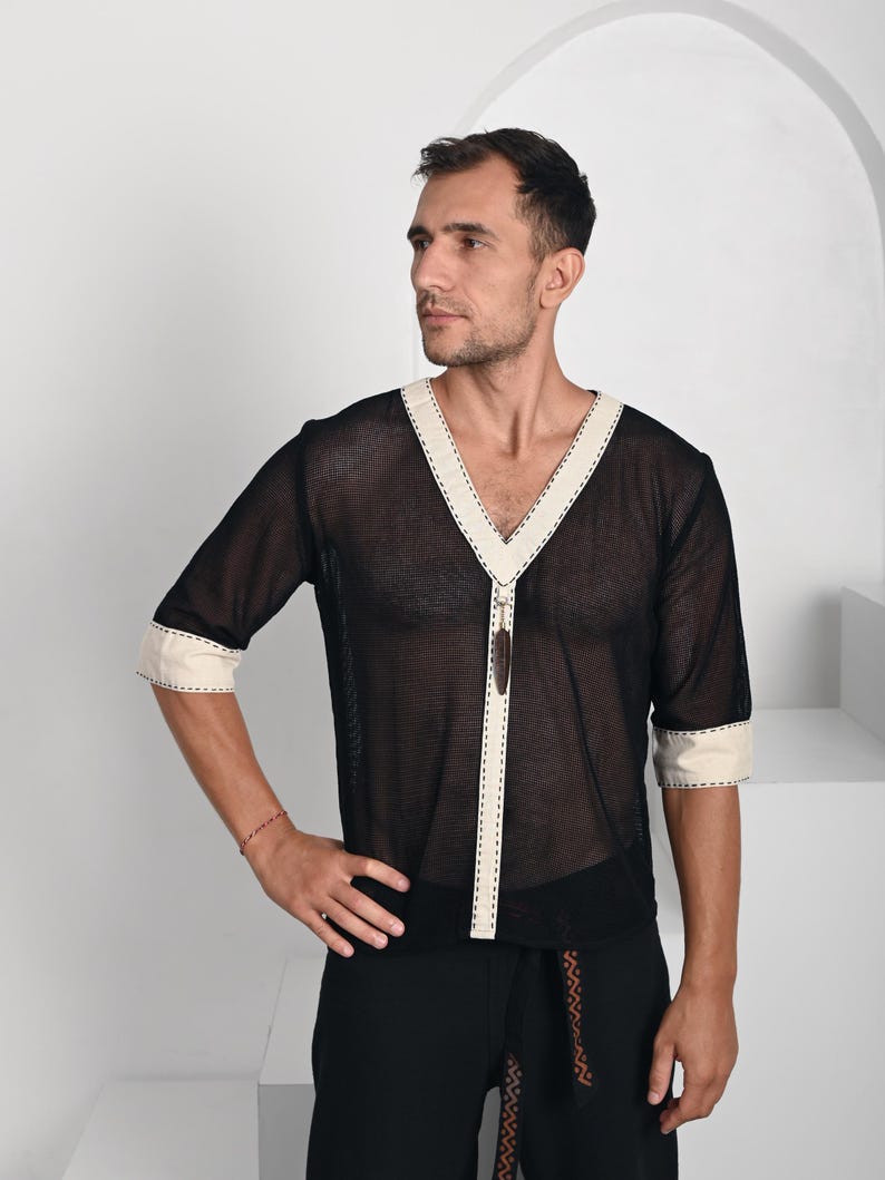 May include: A black mesh shirt with a deep V-neckline and half-length sleeves. The shirt features cream-colored trim along the neckline, front placket, and sleeve cuffs, accented with decorative brown stitching and a small brown pendant detail.