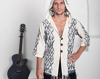 May include: A hooded jacket in off-white featuring a dark gray ikat-style geometric pattern. The garment has three large brown wooden buttons down the front, three-quarter length sleeves, and a fringe hemline at the bottom edge of the jacket.