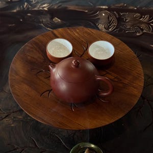 Peut inclure: Un plateau en bois avec une théière brune et deux tasses à thé blanches. Le plateau est posé sur une surface en bois foncé avec un porte-encens vert.