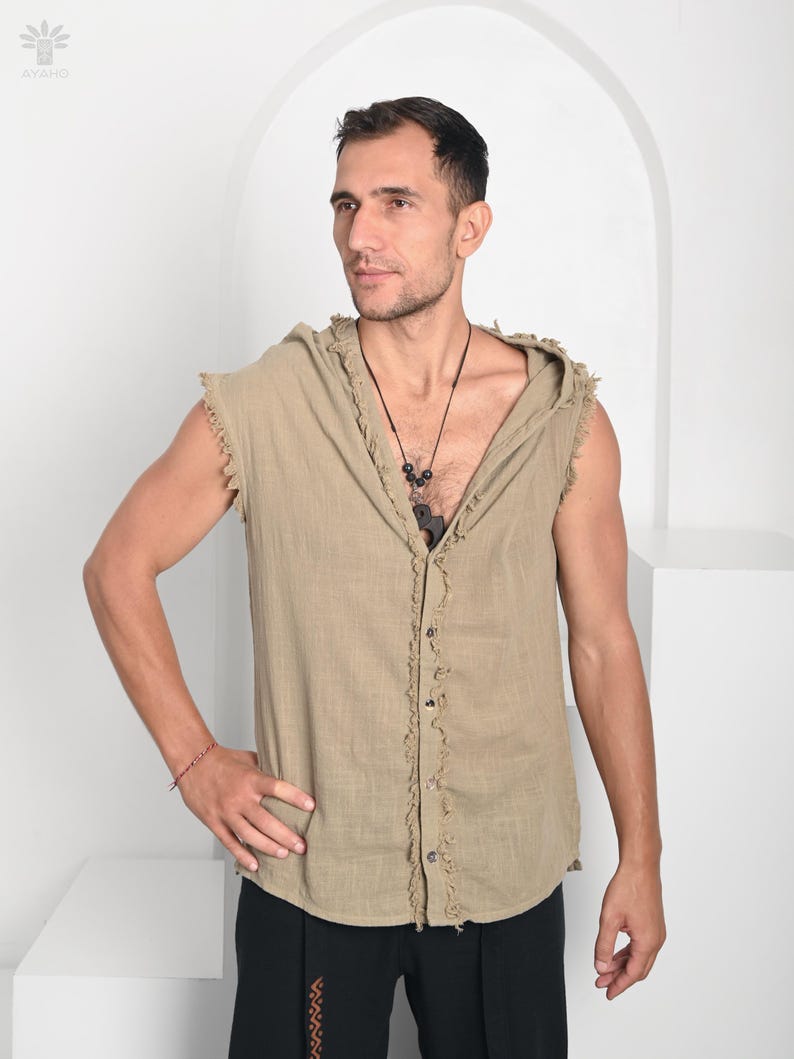 May include: A sleeveless, button-down hooded shirt in a light tan color. The shirt has a frayed edge design along the seams and a relaxed fit. The model is wearing black pants and a necklace. The background is white.