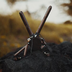 May include: A wooden sculpture with a geometric design, featuring brown and black wood with white beads. The sculpture is resting on a black surface.