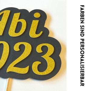 May include: Black and gold glitter paper cutout of "Abi 2023" for a graduation party.