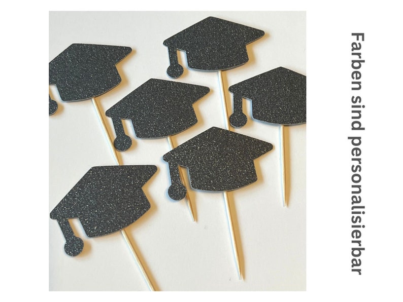 May include: Black glitter graduation cap cupcake toppers on wooden sticks. The image shows several toppers arranged on a white surface. The text on the right side of the image says "Colors are customizable".