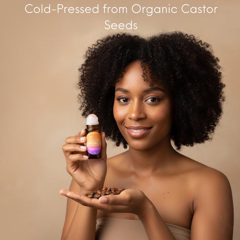 May include: A woman holds a small roller bottle of oil and a handful of castor seeds. The bottle has a colorful label with a gradient design. The text "Cold-Pressed from Organic Castor Seeds" is at the top of the image.