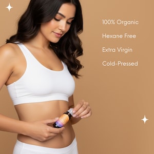 May include: A woman wearing a white sports bra and underwear holds a small, colorful bottle. The bottle has a white cap and a label with orange, purple, and yellow hues. Text on the background reads: 100% Organic, Hexane Free, Extra Virgin, Cold-Pressed.