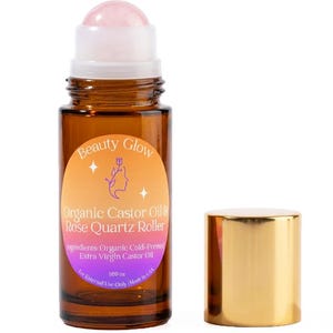 May include: A brown glass bottle with a rose quartz roller and a gold cap. The bottle has a label that reads "Beauty Glow Organic Castor Oil & Rose Quartz Roller." The label also lists ingredients and the volume of 1.69 oz.