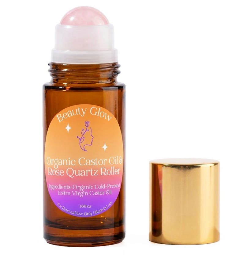 May include: A brown glass bottle with a rose quartz roller and a gold cap. The bottle has a label that reads "Beauty Glow Organic Castor Oil & Rose Quartz Roller." The label also lists ingredients and the volume of 1.69 oz.