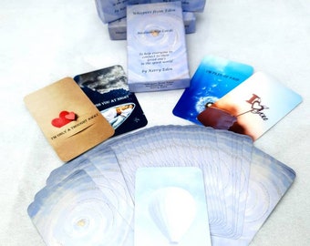 May include: A deck of blue and white oracle cards with a hot air balloon design. The cards have the text "It's so beautiful here" on the front. The back of the cards have the text "Whispers from Eden Mediumship Cards" and "To help everyone to connect to their loved ones in the spirit world by Kerry Eden".
