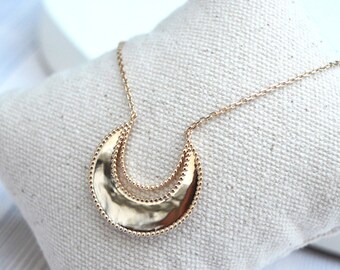 Può includere: Una collana d'oro con un ciondolo a forma di doppia luna crescente. Il ciondolo ha una texture martellata e un bordo perlato.