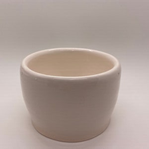 May include: A white ceramic planter with a rounded shape. The planter is empty and ready for a plant.