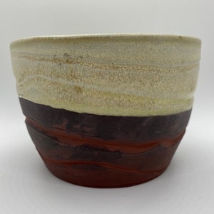 May include: A handmade ceramic bowl with a white glaze on the top half and a brown glaze on the bottom half. The bowl has a slightly rounded shape and a textured surface.