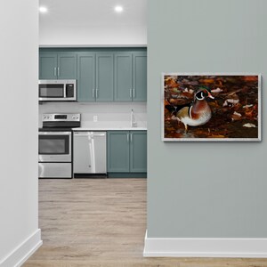 May include: A kitchen with light blue cabinets, stainless steel appliances, and a wood floor. A framed print of a wood duck in a fall setting hangs on the wall.