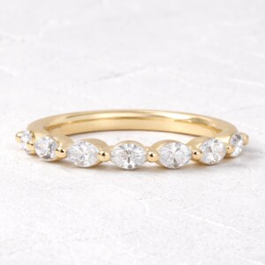 May include: A gold ring with a series of clear, round-cut gemstones. The ring has a polished, yellow-gold finish and the gemstones are evenly spaced along the band. The ring is set against a white background.