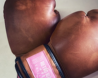May include: A pair of brown leather boxing gloves with black trim and a pink patch that says "Retro Reborn x Pro Box Collection".