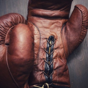 May include: A pair of brown leather boxing gloves with black laces. The gloves have a tag that says "Retro Reborn" with a logo of two crossed "R"s.