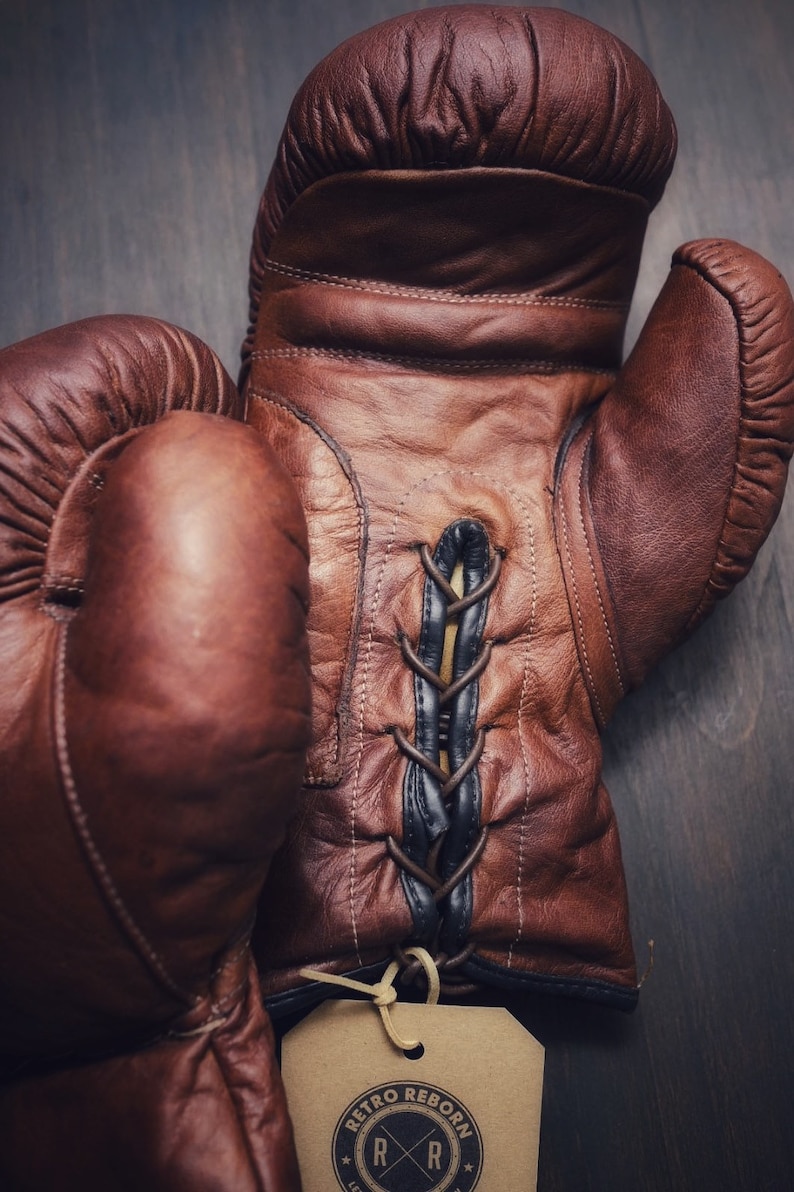 May include: A pair of brown leather boxing gloves with black laces. The gloves have a tag that says "Retro Reborn" with a logo of two crossed "R"s.