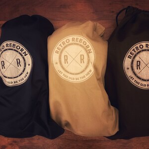 May include: Three drawstring bags in black, beige, and dark brown with a white logo that reads "Retro Reborn" and features a stylized "RR" with a star on either side. The logo also includes the text "Let the old be the new".