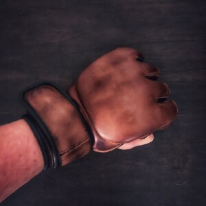 May include: A brown leather boxing glove with a black wrist strap. The glove is worn and has a distressed look.