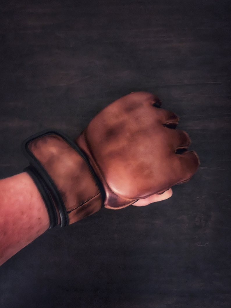 May include: A brown leather boxing glove with a black wrist strap. The glove is worn and has a distressed look.