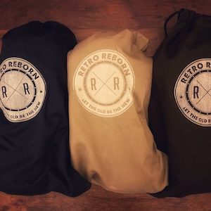May include: Three drawstring bags in black, beige, and dark brown with a white logo that reads "Retro Reborn" and features a stylized "RR" with a star on either side. The logo also includes the text "Let the old be the new".