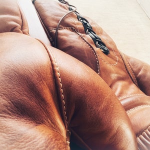 May include: A pair of brown leather boxing gloves with white stitching. The gloves are laced together with a black braided cord.