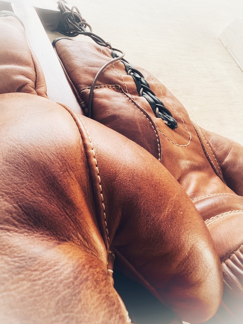 May include: A pair of brown leather boxing gloves with white stitching. The gloves are laced together with a black braided cord.