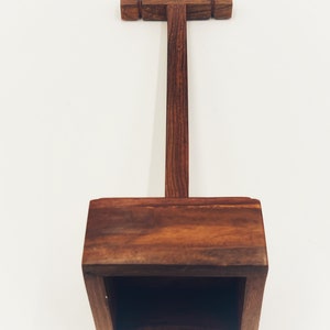 May include: A wooden headphone stand with a square base and a T-shaped top. The stand is made of dark brown wood.